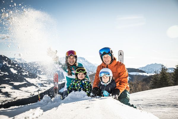 Familie mit zwei kleinen Kindern in Schneeanzügen sitzt in den Bergen im Schnee