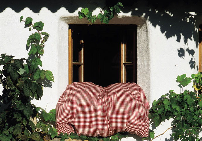 Tuchent hängt über das Fensterbrett eines Bauernhauses, im Vordergrund Holzscheite